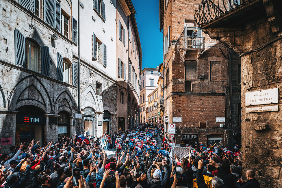 Gledaoci u uskoj ulici u italijanskoj Sijeni gledaju bicikliste dok voze 12. etapu takmienja iro d' Italija 2021. godine/Ashley & Jered Gruber